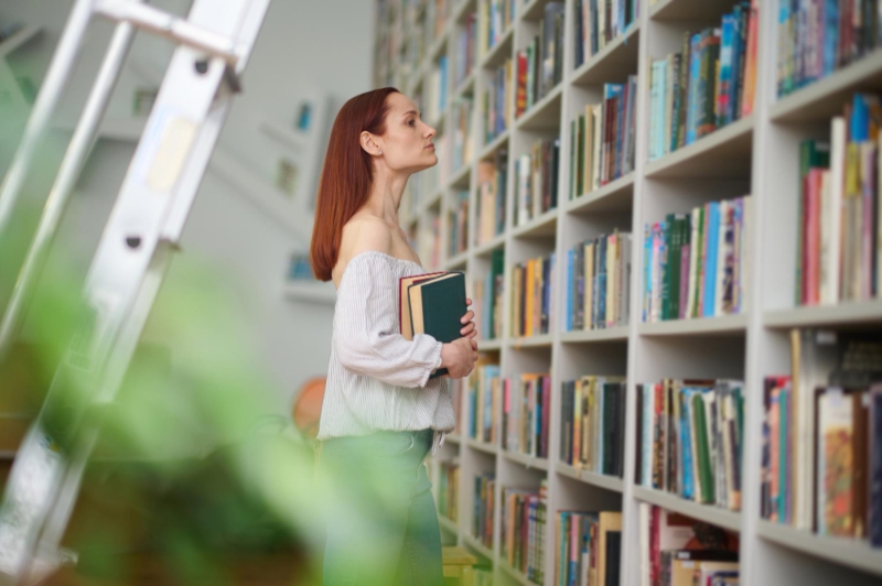 Mujer en bilbioteca mirando libros. Hábito de lectura.